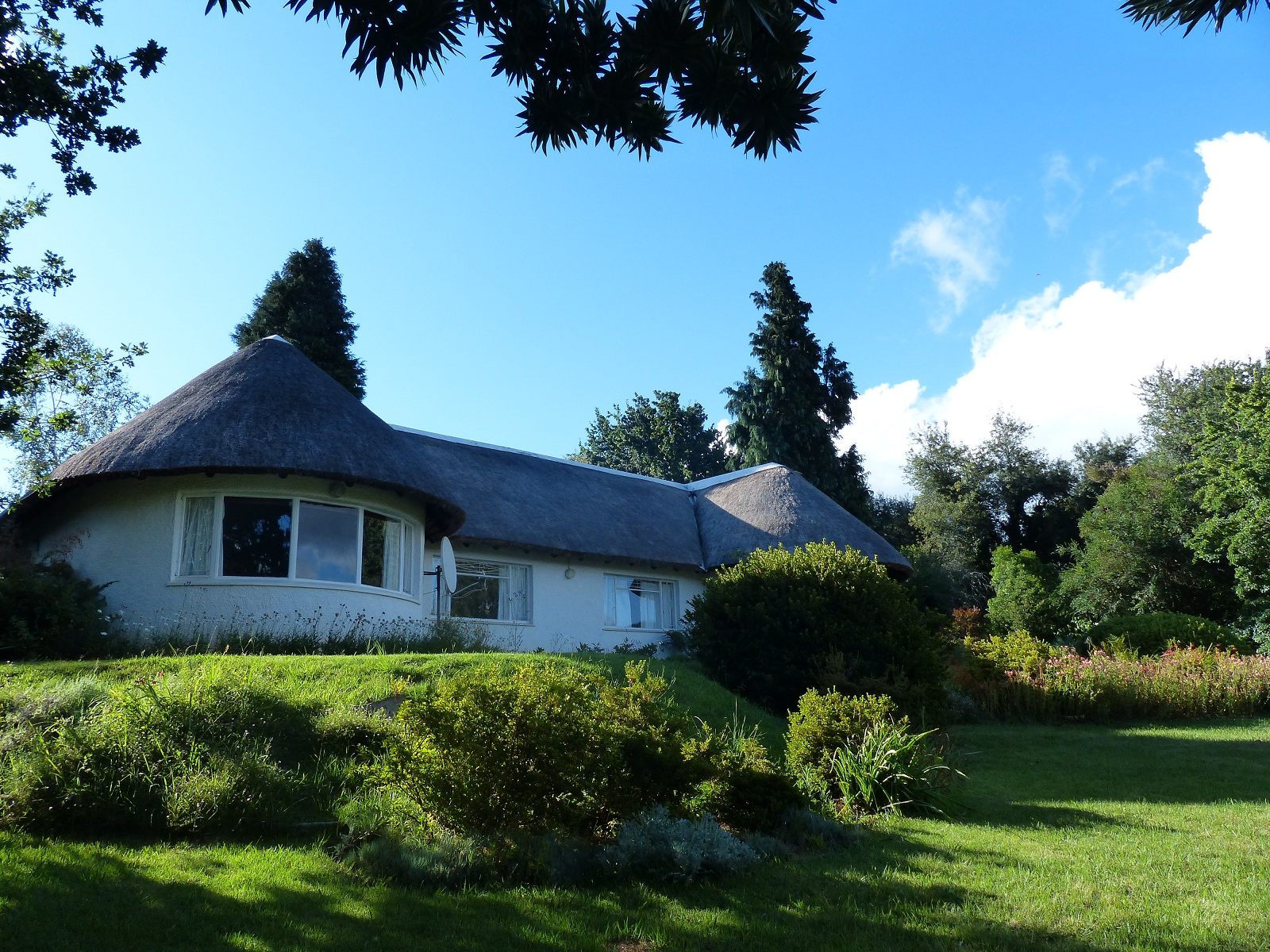 The thatched Main House among the garden and trees